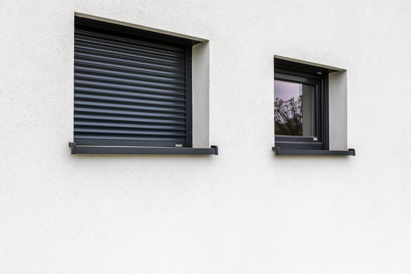 Grey roller shutter over a small window in a white wall