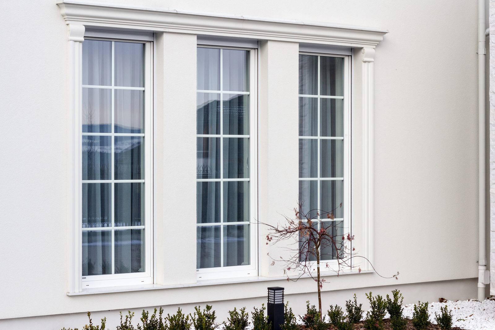 Three tall white windows with glazing bars on a rendered wall