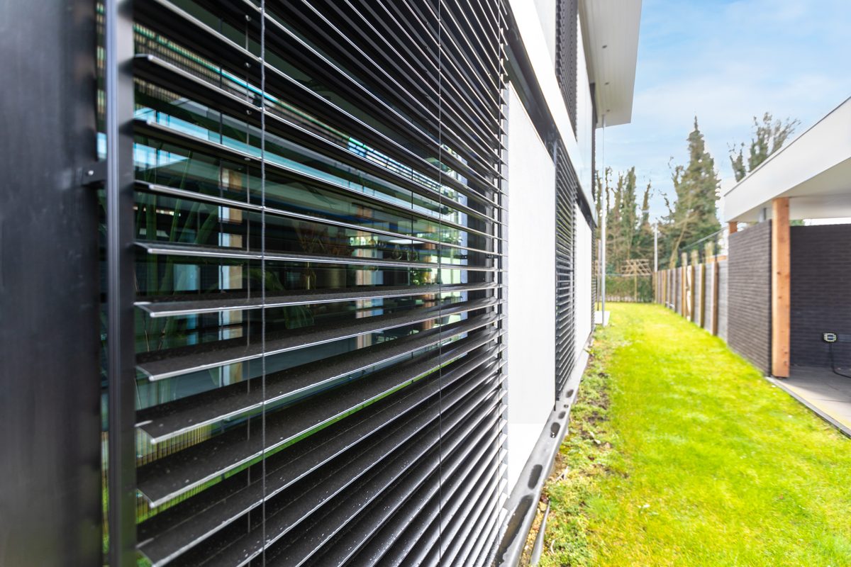 Black venetian blinds along the side of a modern white house